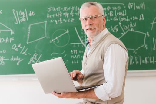 Professor holding a laptop in front of a blackboard